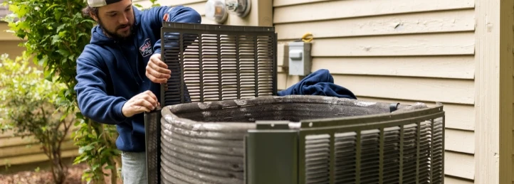HVAC technician opening and inspecting an outdoor air conditioning condenser unit beside a house.