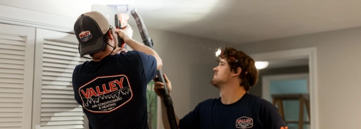 Two HVAC technicians installing or servicing ductwork near a ceiling vent inside a home.